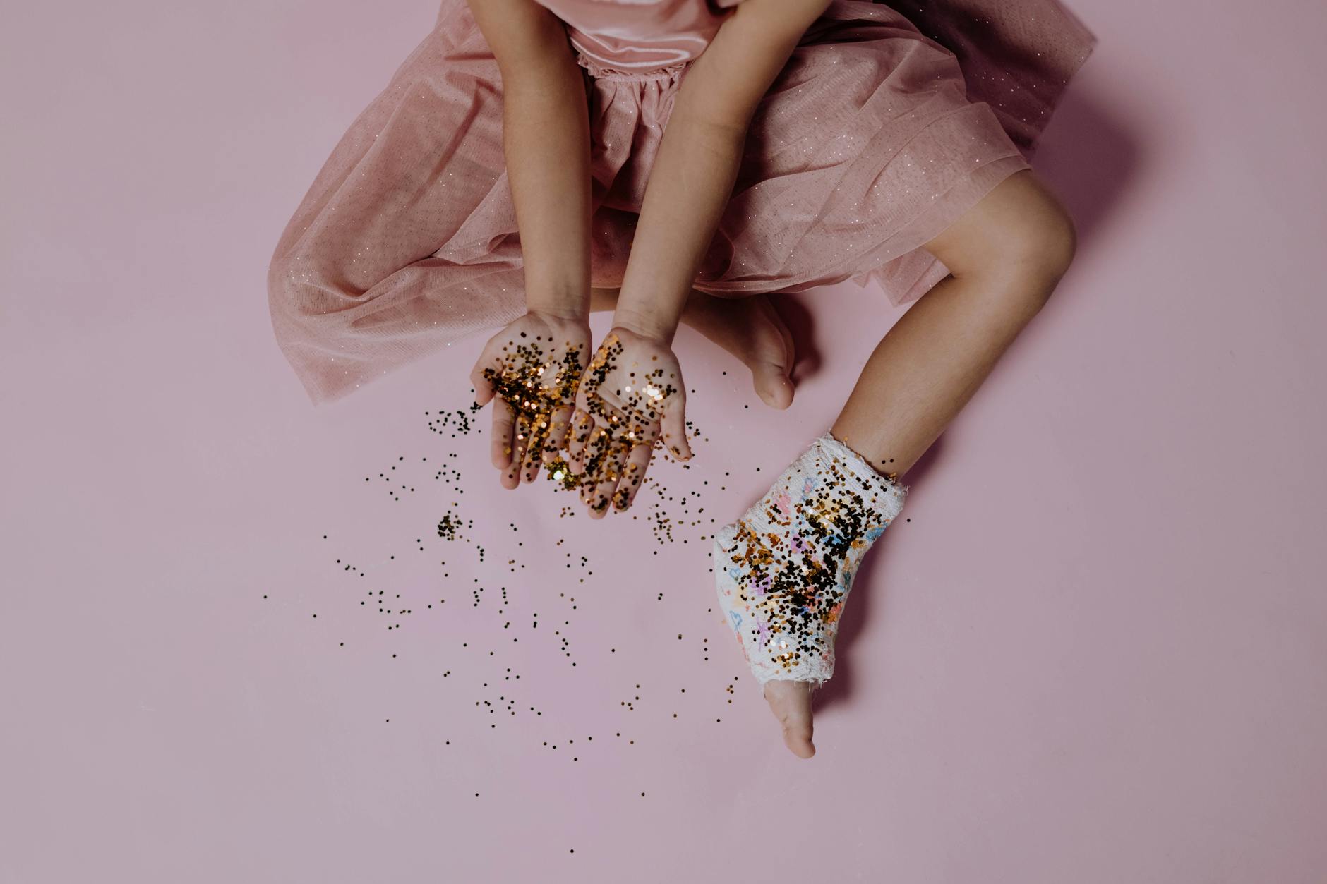 top view of a little girl with her foot in a cast holding golden glitter in hands