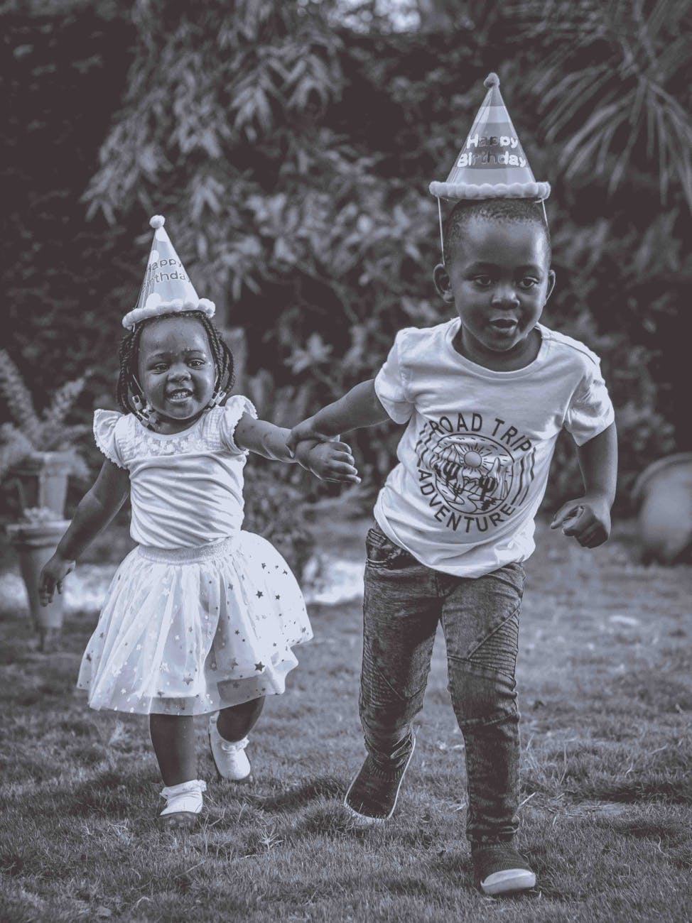 grayscale photo of kids wearing party hats while running on the grass