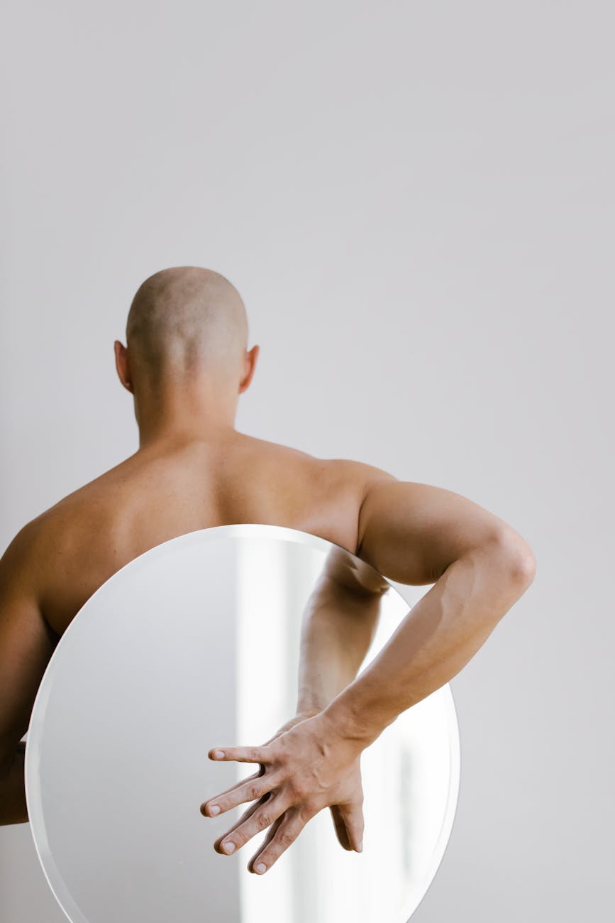 topless man holding white round mirror from his back