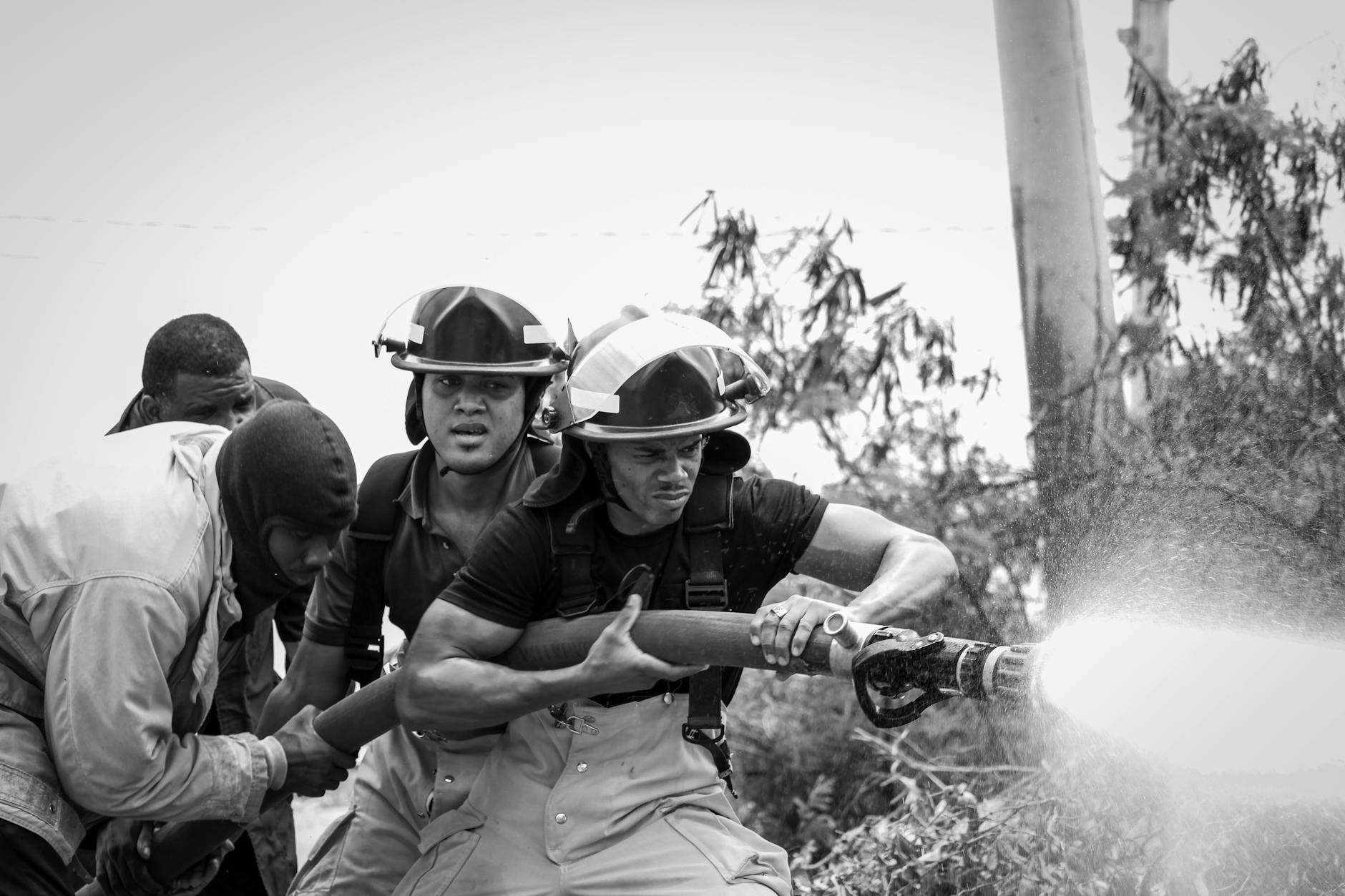 a grayscale photo of firefighters holding a fire hose