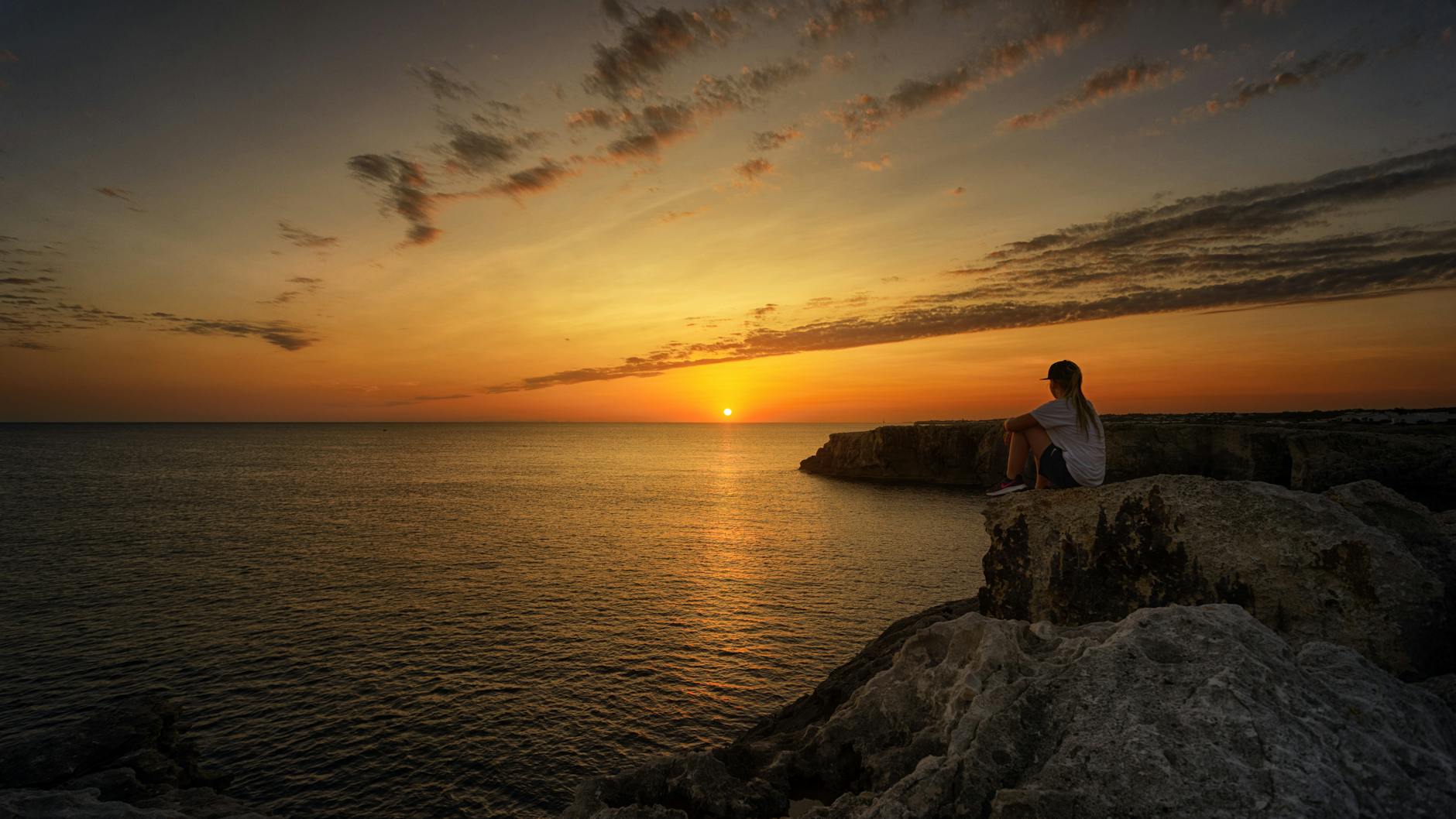 photo of person sitting on rock during sunset