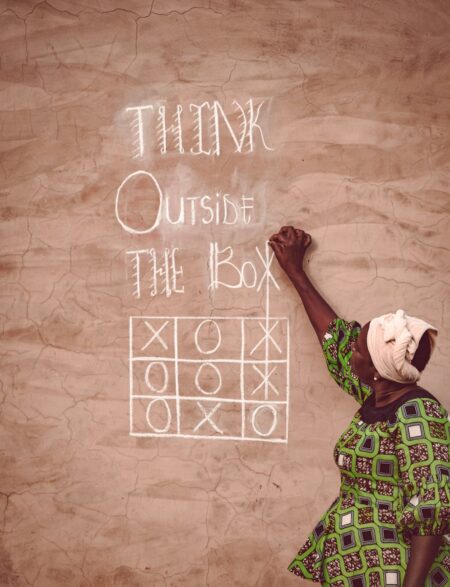 woman wearing a green patterned dress writing noughts and crosses with a chalk on a wall