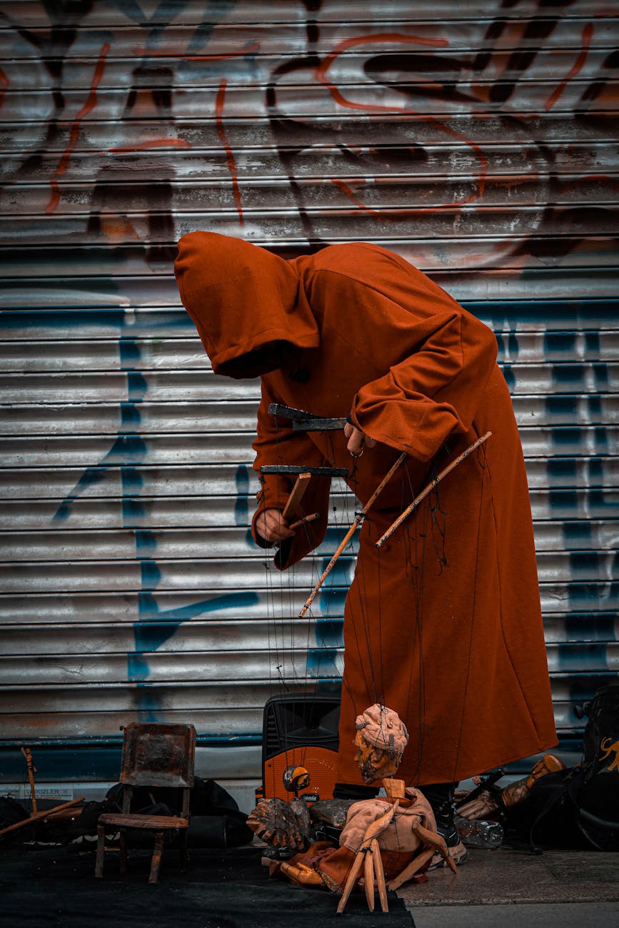 person in robes with hood standing with puppets