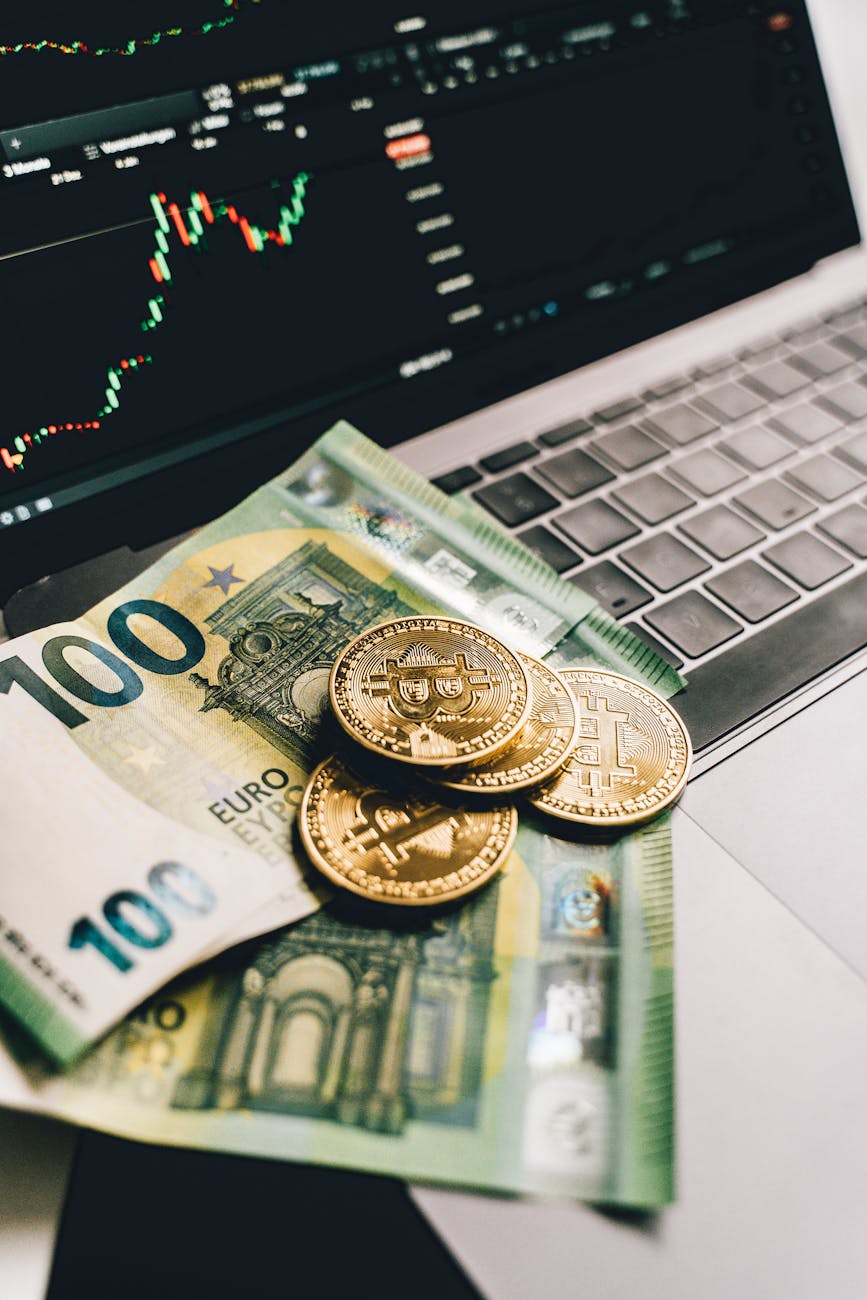 bitcoins and paper money on a laptop with graph on screen