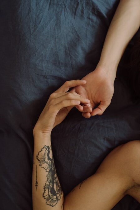 two persons lying in bed while holding hands