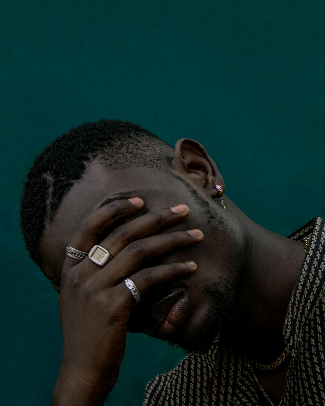 close up photo of a man covering his face with his hand with rings