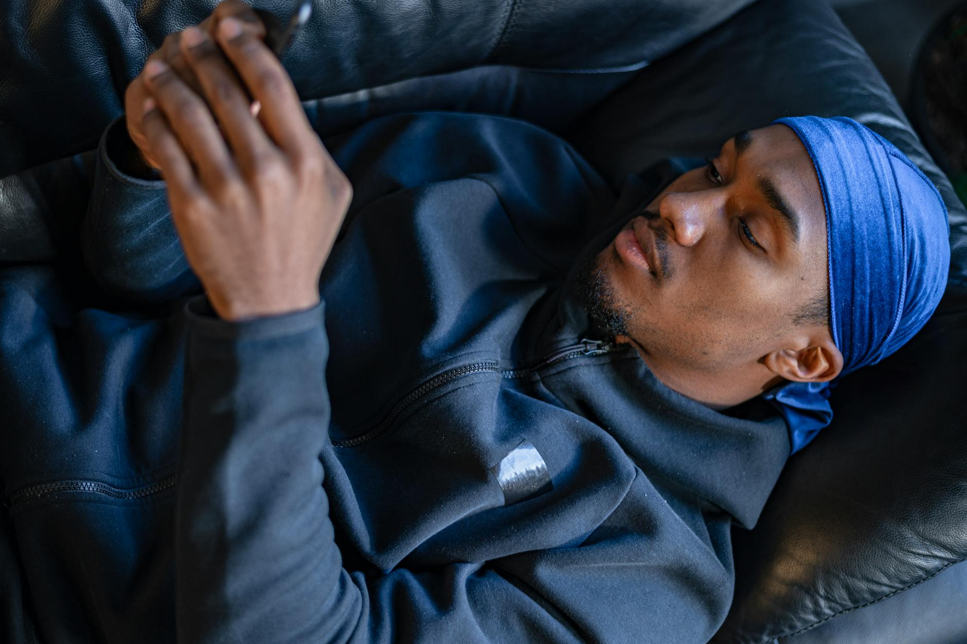 man in dark blue jacket lying on couch using smartphone