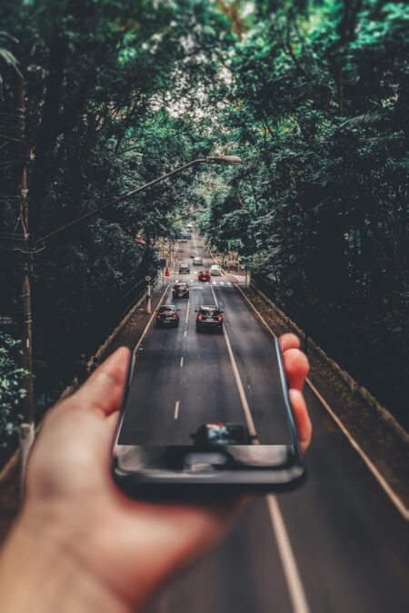 forced perspective photography of cars running on road below smartphone