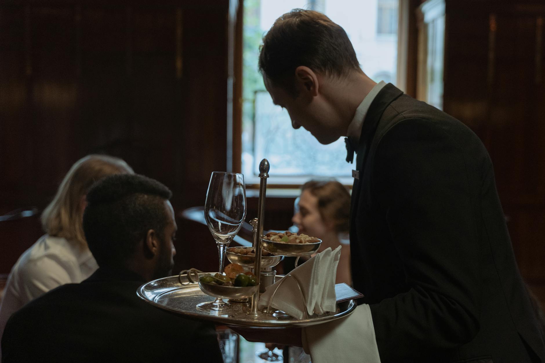 a man in black suit serving foods while holding a stainless tray
