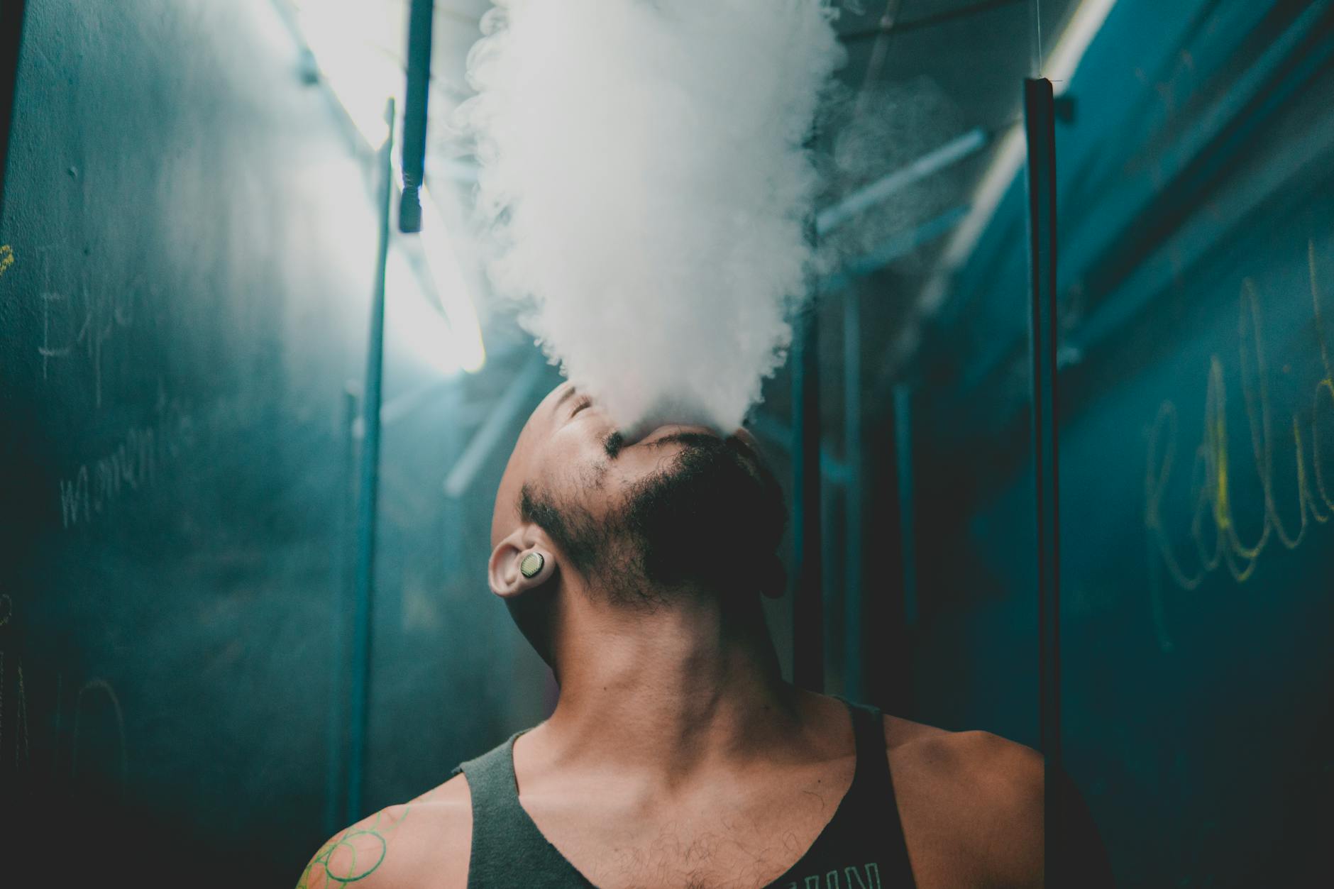a bearded man in a tank top blowing smoke