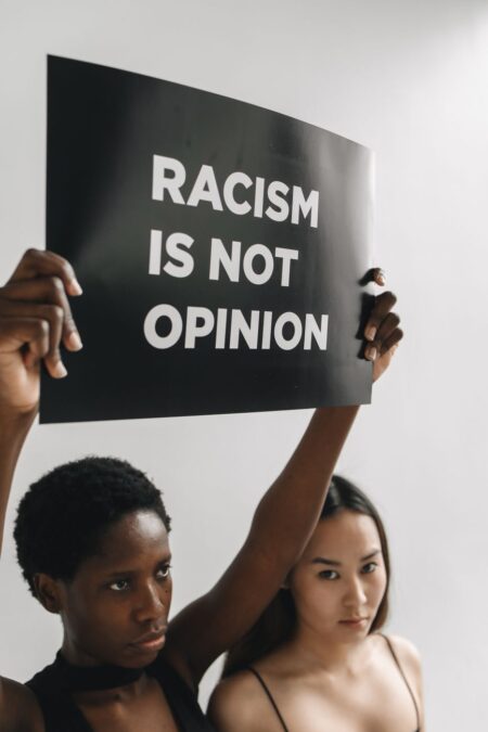 woman holding a black placard with message while standing next to another woman