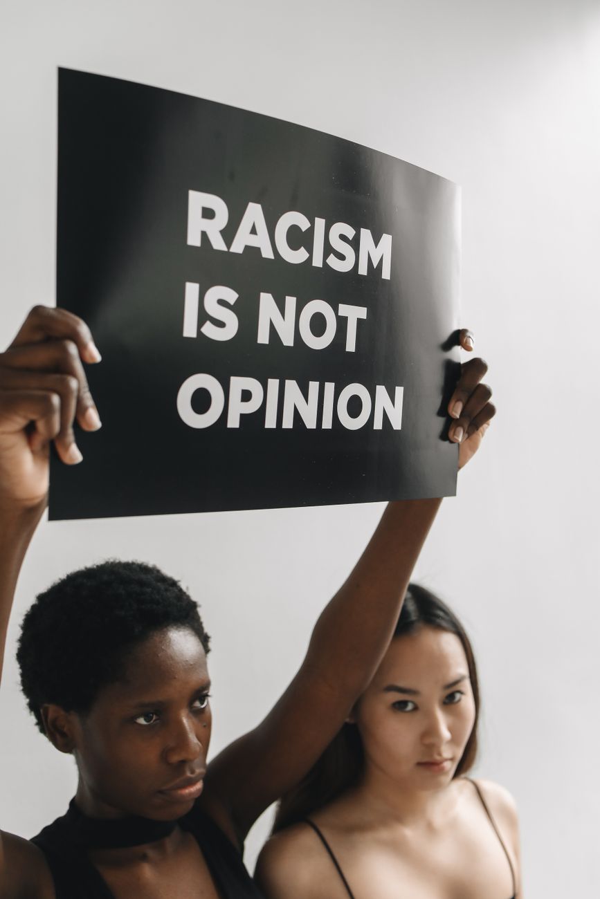 woman holding a black placard with message while standing next to another woman